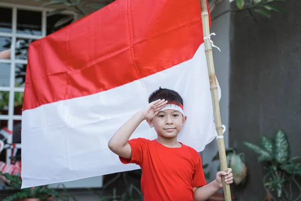 Anak asia memberi hormat sambil memegang bendera indonesia — Stok Foto