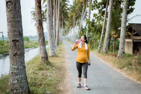 Беременная женщина пьет бутылку воды во время тренировки — стоковое фото