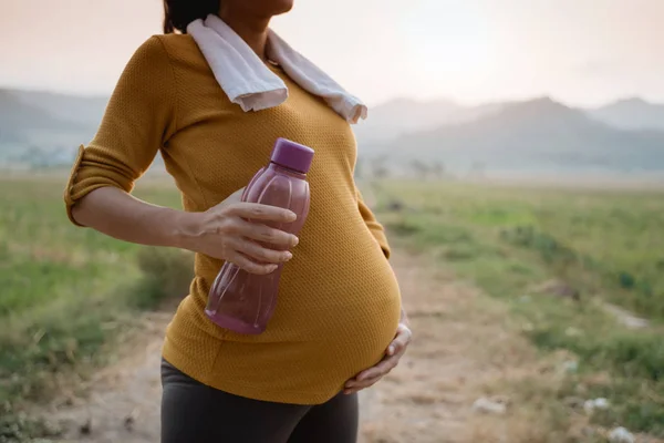 Vientre embarazada con botella de agua mientras hace ejercicio —  Fotos de Stock