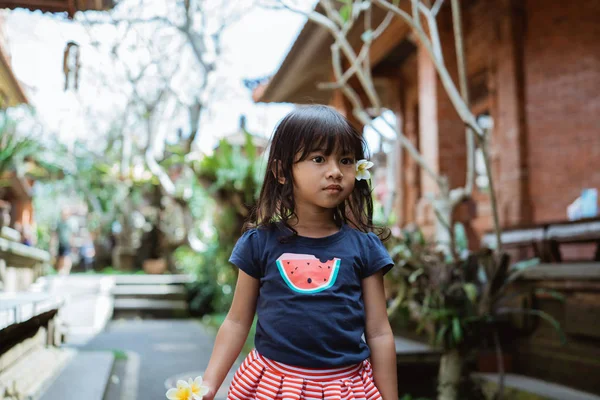 Liten flicka som bär blomma i örat går utanför i huset — Stockfoto