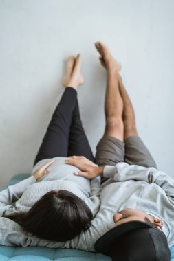 Asya çift elleri ile kanepede rahatlatıcı göbek eşi hamile tutun