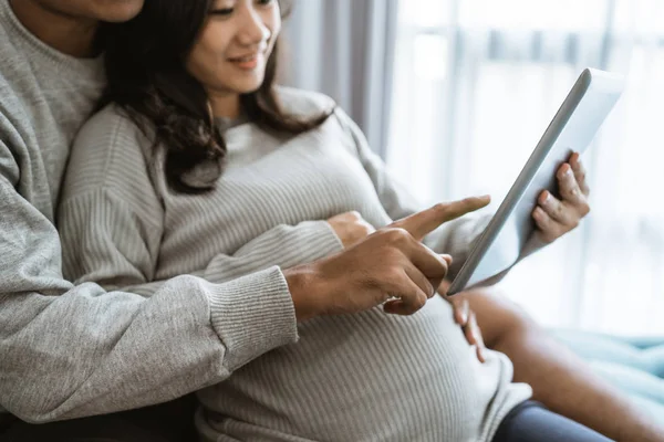 Geluk van koppels houden de vrouws zwangere maag tijdens het gebruik van digitale Tablet — Stockfoto