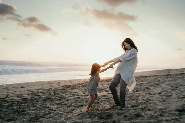 Young beautiful pregnant woman with her little cute daughter playing in the beach — Stock Photo, Image