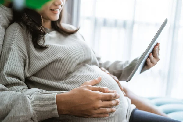 Felicidad de las parejas que sostienen a las esposas embarazadas estómago mientras se utiliza la tableta digital —  Fotos de Stock
