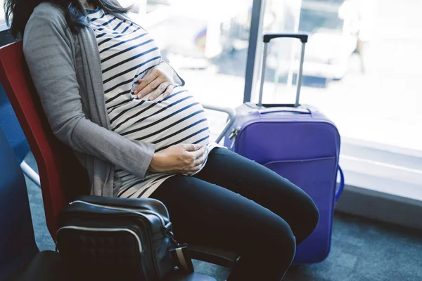 Беременная азиатка сидит рядом с чемоданом — стоковое фото