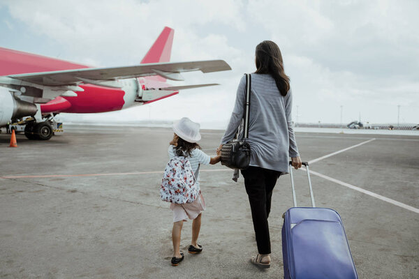 Маленькая девочка и мама держатся за руки, идут к самолету
