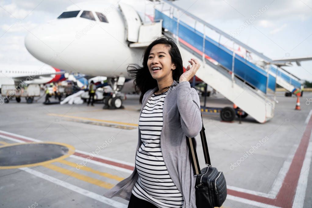 asian pregnant woman standing pulling suitcase