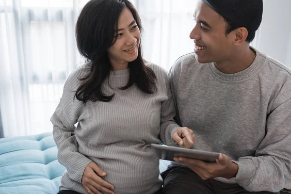 young romantic couple sitting on the couch while holding digital tablet