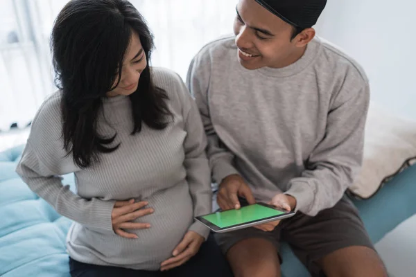 Een zwangere vrouw en echtgenoot zittend terwijl hij een digitale Tablet vasthoudt — Stockfoto