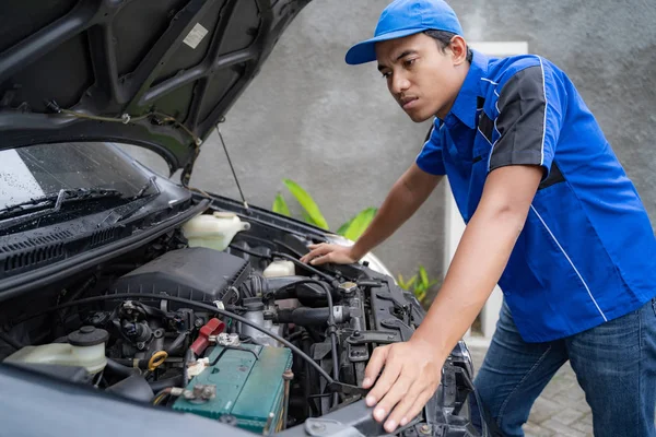 Инженер в синей униформе, изучающий двигатель автомобиля — стоковое фото