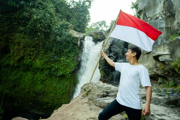 Pria dengan bendera indonesia di air terjun dengan pemandangan indah — Stok Foto