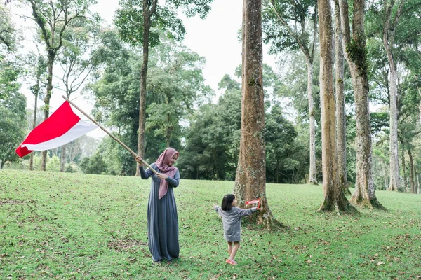 Indonezyjska hidżab kobieta trzyma bambusowy kij z wielką flagą — Zdjęcie stockowe