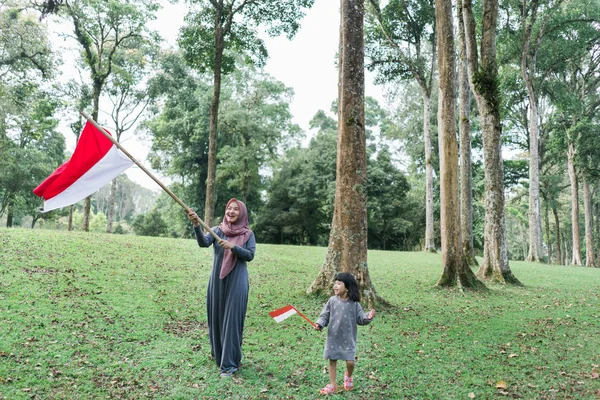 Aziatische gesluierde moeder wit dochter flappen Indonesische vlag — Stockfoto