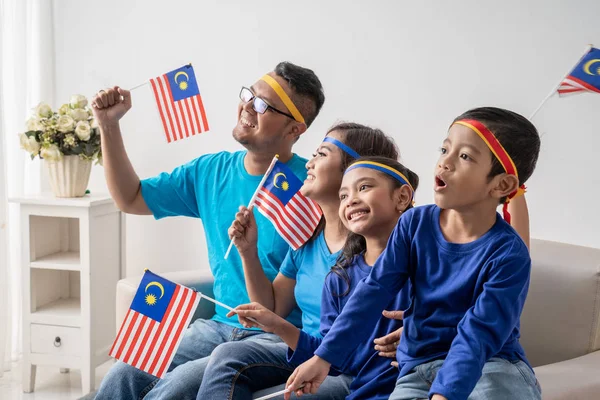 Keluarga dengan bendera malaysia duduk di sofa menonton sepak bola — Stok Foto