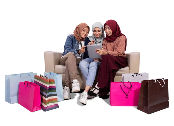 Tres mujeres veladas sentadas cerca de bolsas de papel y con tarjeta de crédito para comprar en una tienda en línea — Foto de Stock