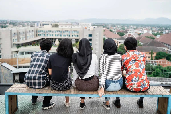 Bakifrån av unga vänner sitter tillsammans på taket — Stockfoto