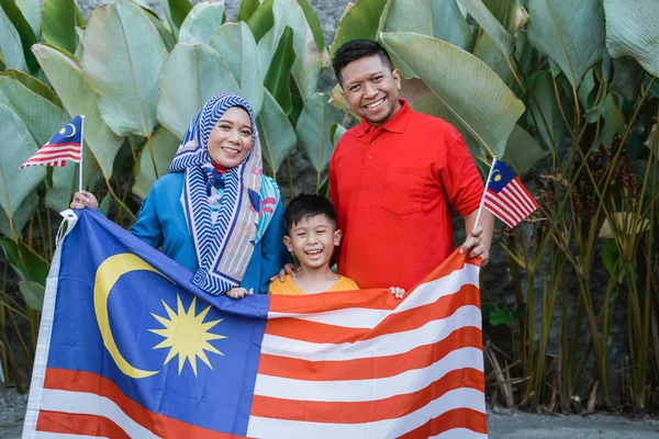 malaysian family holding malaysia flag in front of their house