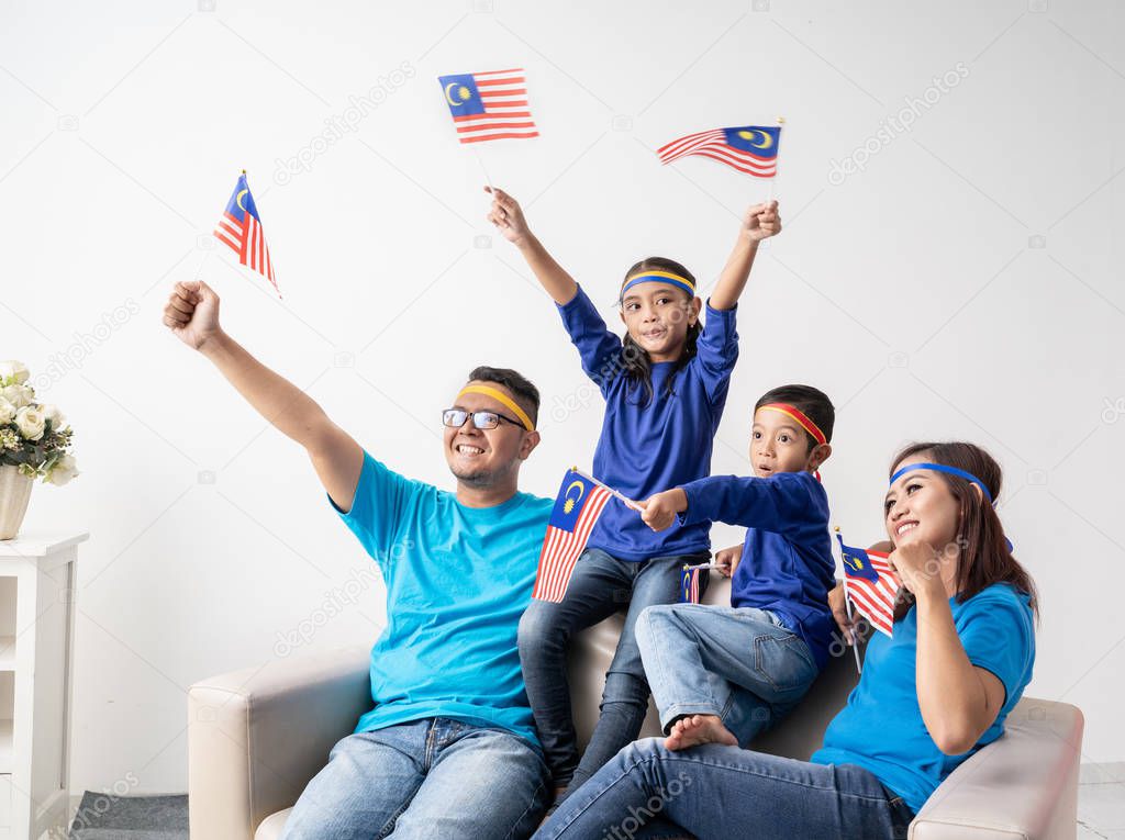 family with malaysia flag sitting on a couch watching soccer