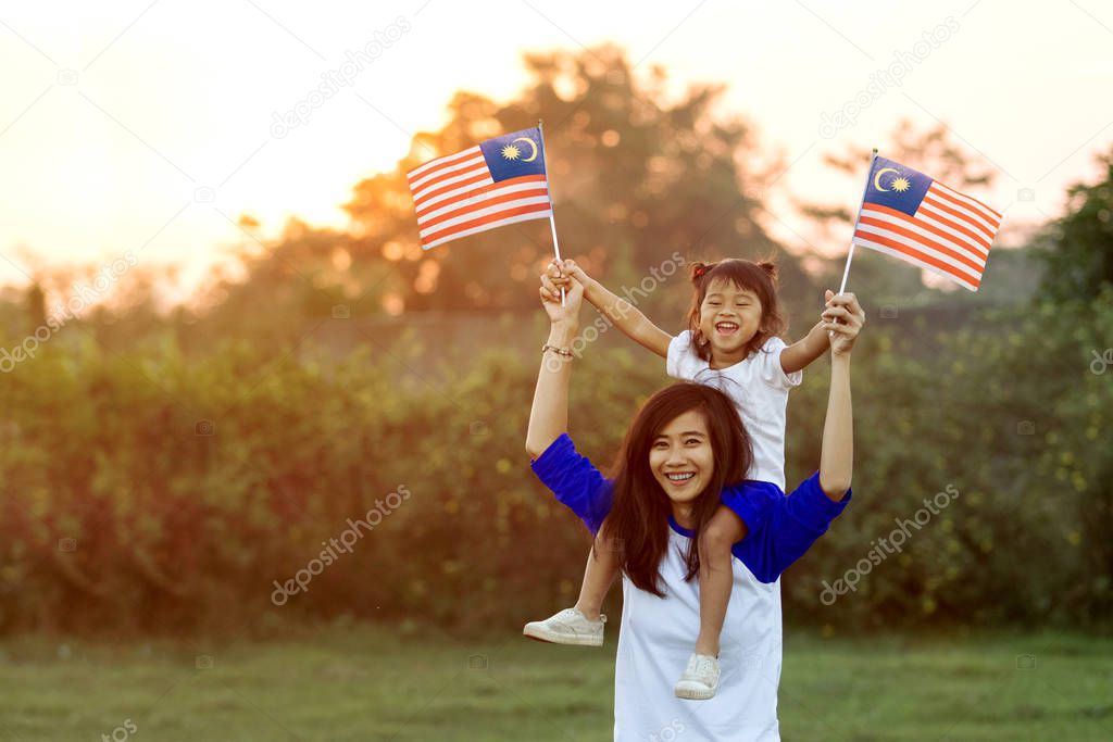 mother and daughter raising flag of malaysia