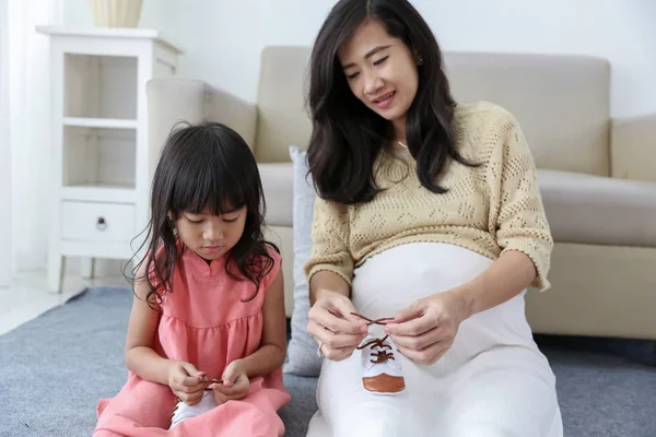 Hija está arreglando los cordones de los zapatos de los bebés con su madre embarazada —  Fotos de Stock