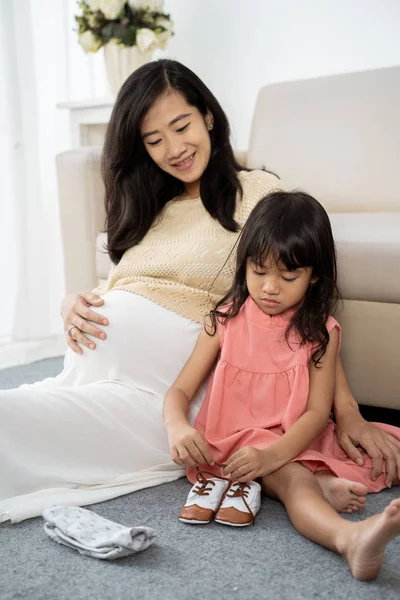 Asiático chica es la fijación el babys shoelaces con su embarazada madre —  Fotos de Stock