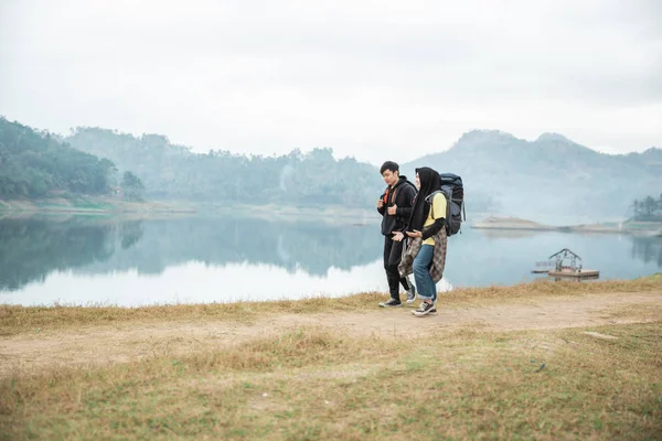 Pareja de excursionistas con mochilas caminando lado del lago — Foto de Stock