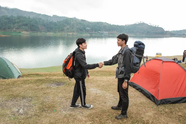 Dois homens caminhantes se encontram perto do lago com a mão apertada — Fotografia de Stock