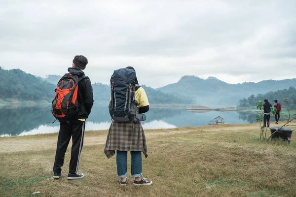 Caminhantes casal com mochilas desfrutando vista lago — Fotografia de Stock