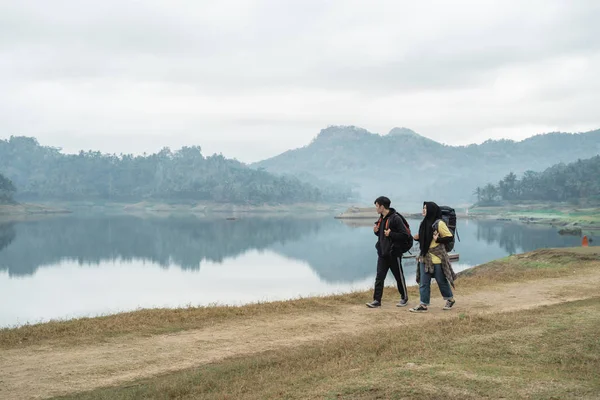 Pareja de excursionistas con mochilas caminando lado del lago — Foto de Stock