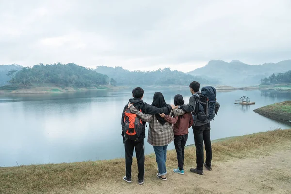 Viaggiatori con zaini che si affacciano godere della vista sul lago dal prato — Foto Stock