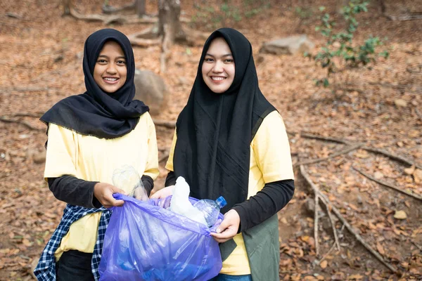 Two woman hijab smiling volunteer holding trash bag