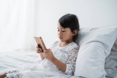 yatakta cep telefonu kullanarak asyalı kız çocuk