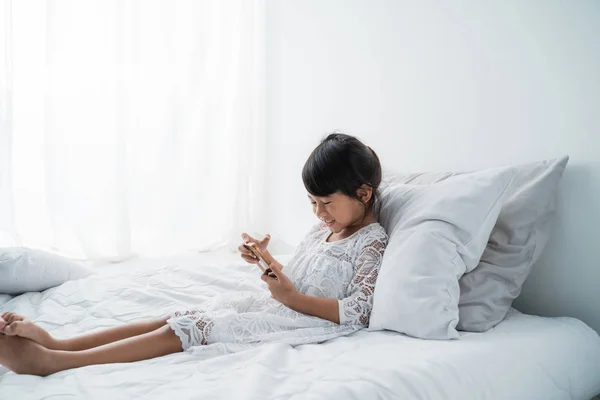 Aziatische meisje kind met behulp van mobiele telefoon op bed — Stockfoto