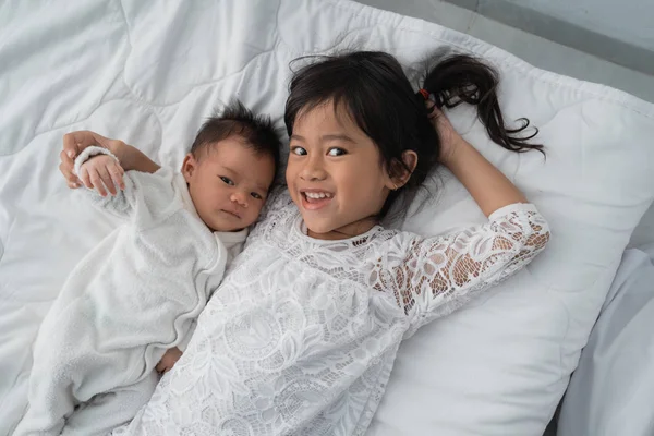 Filha criança com bebê irmão brincando na cama vestindo branco — Fotografia de Stock
