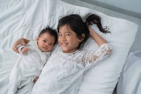 Dotter Kid med spädbarn syskon spela på sängen klädd i vitt — Stockfoto