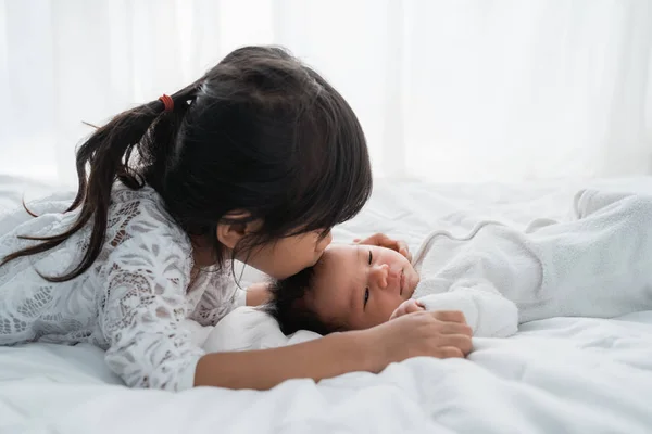 Daughter kid with infant sibling playing on bed wearing white — Stock Photo, Image