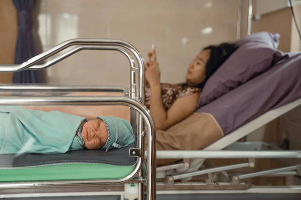 Baby układanie w łóżeczku z matką za pomocą telefonu komórkowego r. po stronie łóżka — Zdjęcie stockowe