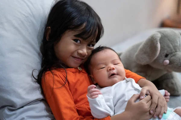 Ältere Schwester lächelt und umarmt ihre kleine Schwester — Stockfoto