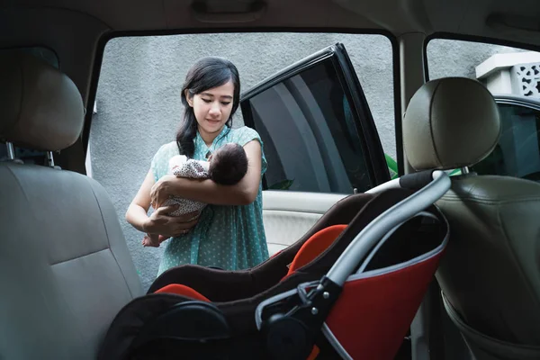 車の安全シートに入る前に娘を運ぶ若い母親 — ストック写真