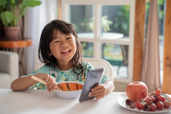 Bambino godere la sua colazione tenendo lo smartphone — Foto Stock