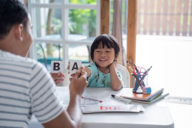 Baba, yeni yürümeye başlayan çocuğa okuma yazma öğretiyor.