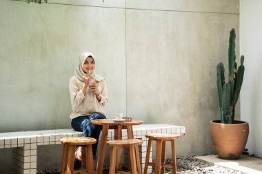 Peçeli kadın gülümsemesi, elinde bir bardak buzlu kahve.