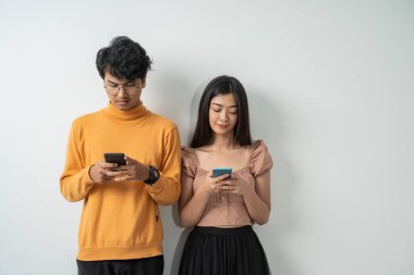 Asyalı genç çiftler ayakta dururken akıllı telefonlarını kullanıyorlar.