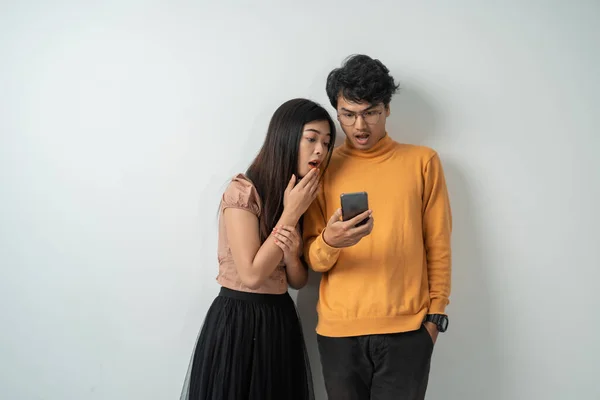 Νεαρό ζευγάρι ασιατών στάθηκε κοιτάζοντας την οθόνη ενός έξυπνου τηλεφώνου με μια εκπληκτική έκφραση — Φωτογραφία Αρχείου