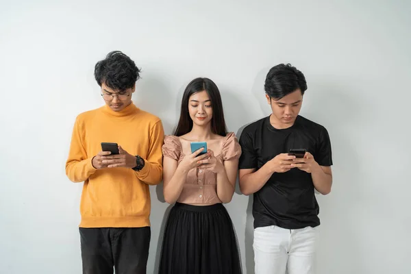 Tre giovani asiatici usano i loro smartphone mentre sono in piedi — Foto Stock