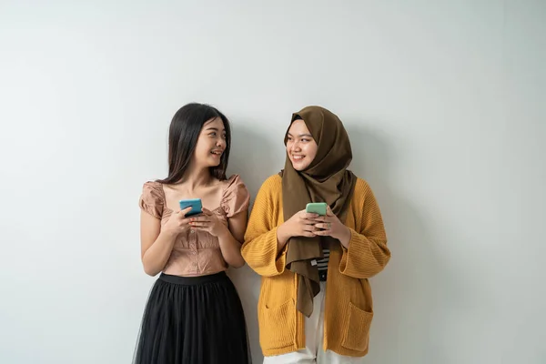 Twee vriendelijke meisjes kijken elkaar aan terwijl ze hun smartphones gebruiken — Stockfoto