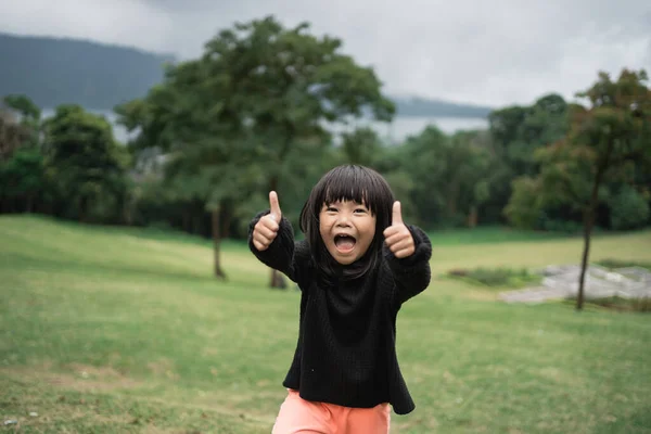 Liten asiatisk flicka skrattar medan du visar tummen upp — Stockfoto