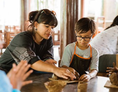 Çocuk annesiyle kil oynarken önlük takıyor.