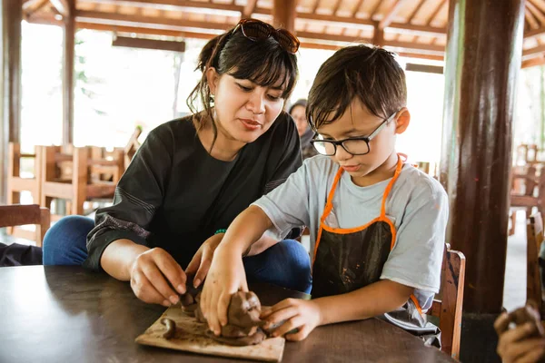 Niño usando un delantal hace artesanías de barro con su madre — Foto de Stock