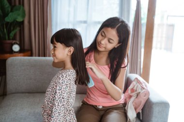 Kardeşinin saçını taramasına yardım eder.